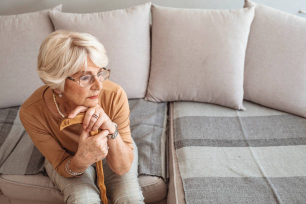 istock Senior woman sitting on sofa and holding walking stick. 1285143649