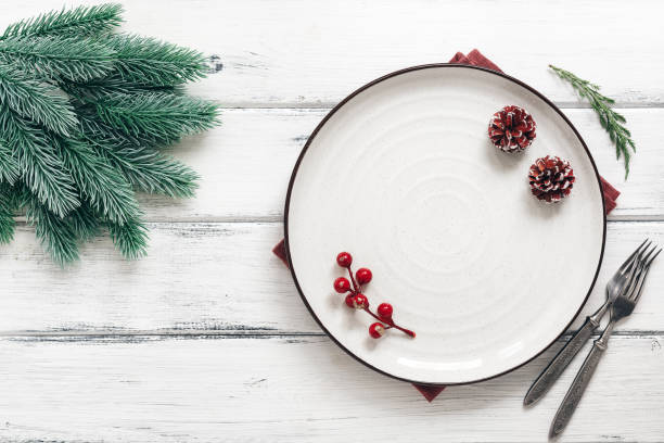 istock Christmas table setting. Empty white plate and spruce branch on a white wooden table. Top view, flat lay. 1285143800