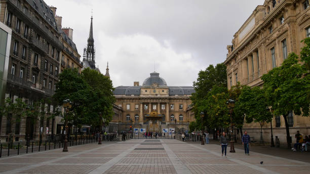 Front view of historic Palais de Justice ("palace of justice") with tourists walking by on a pedestrian zone framed by trees and old buildings. stock photo