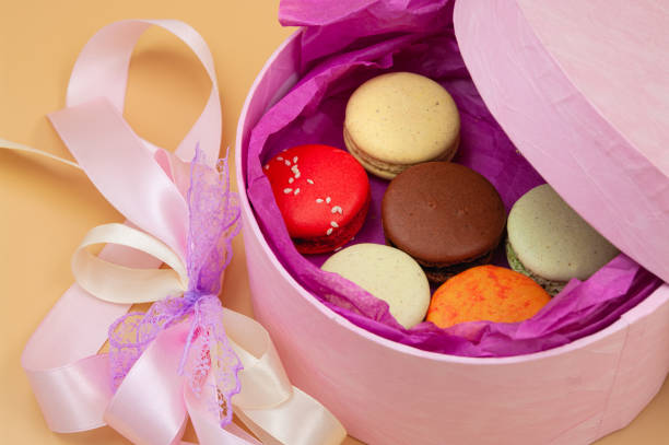 Four brightly colored French Macarons in pink cardboard box on peach background
