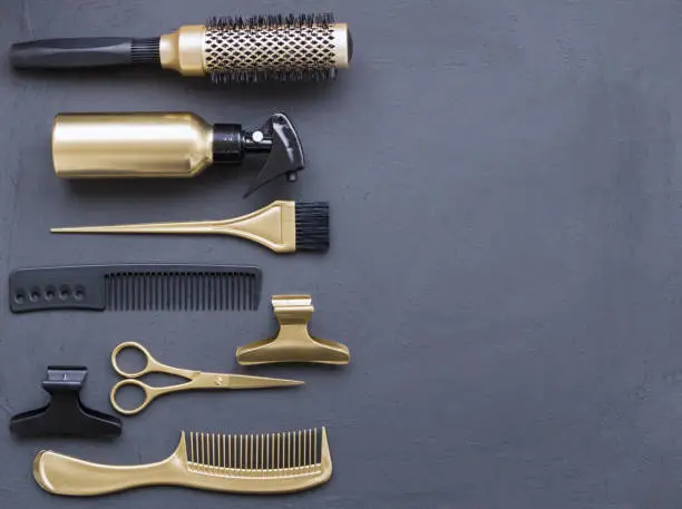 Photo of Hairdressing tools in black and gold on a gray concrete background. Hair salon accessories, combs, scissors and hair clips in the corner and with copy space.