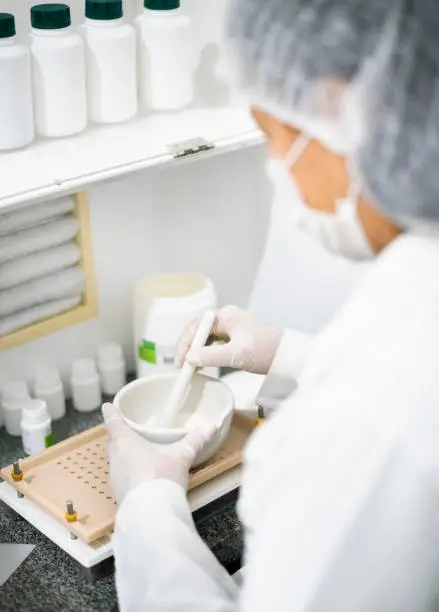 Female chemist mixing medicine in mortar pestle in the pharmacy laboratory