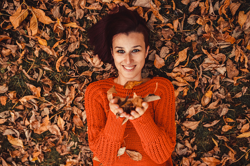 Young woman lying and playing in autumn leaves heap.