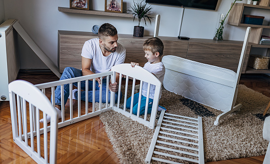 Father and son sitting on the floor and making baby crib together in the living room