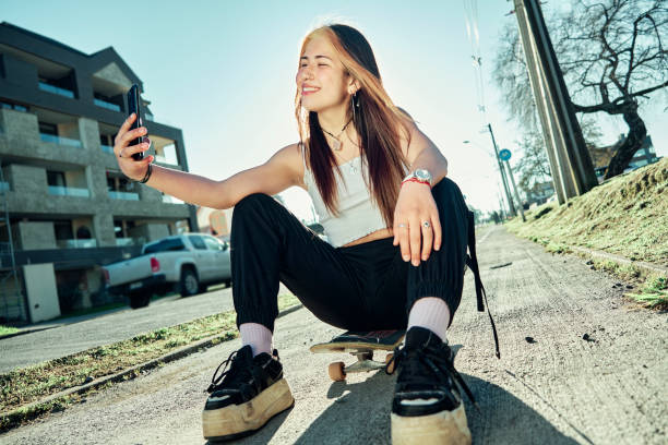istock Young girl sitting on a skateboard on a bicycle path and taking a selfie 1285165134