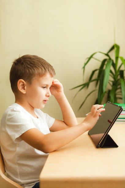 istock Cute child doing homework with tablet sitting by desk 1285167516