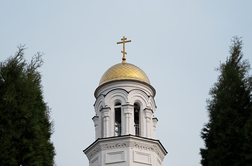 The white church with the golden dome close-up between the trees