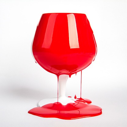 red paint pouring on white objects- apple and wineglass. Artistic concept.