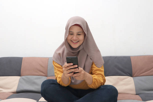 istock Beautiful Asian muslim woman using phone while sitting on sofa, girl doing chat message on smartphone and smiling 1285171780