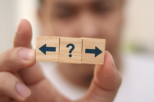 Choosing direction concept, man holding wooden block with arrow and question mark symbol, selective focus
