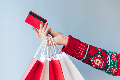 Close up crooped shot of woman hand holding many paper handbags and red credit card