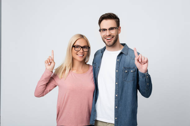 istock Smiling couple in eyeglasses pointing with fingers isolated on grey 1285176377