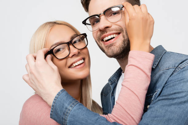istock Smiling couple looking at camera while touching eyeglasses of each other isolated on grey 1285176378