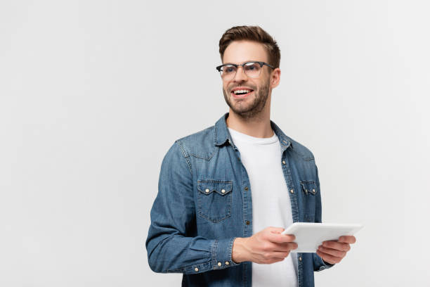 istock Smiling man in eyeglasses holding digital tablet isolated on grey 1285176438
