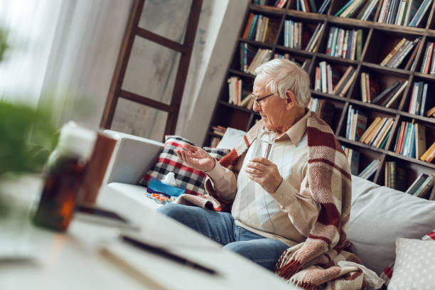 istock Senior man alone sitting at library sick covered with plaid looking at pills 1285181775