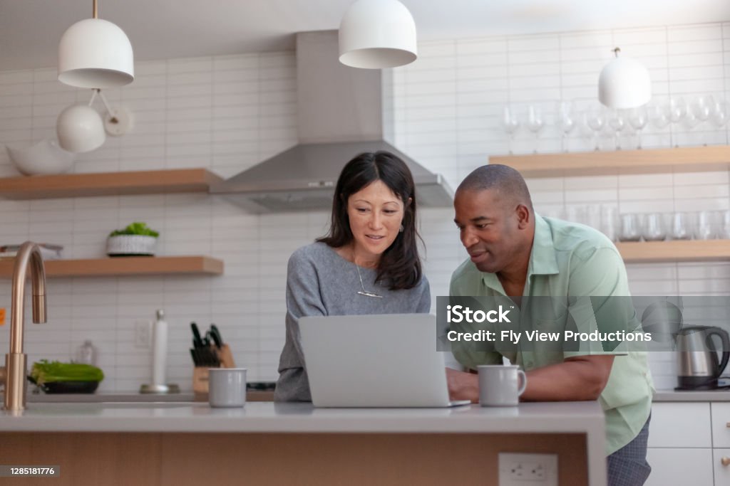 Husband and wife working on taxes A mixed race couple use a laptop computer to pay bills online, manage budget and prepare tax documents. They are in the kitchen of their home. Couple - Relationship Stock Photo