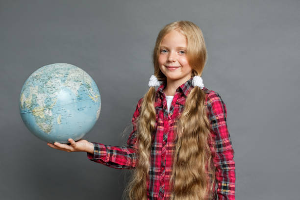 istock Little girl with ponytails standing isolated on grey with globe looking camera friendly 1285181797