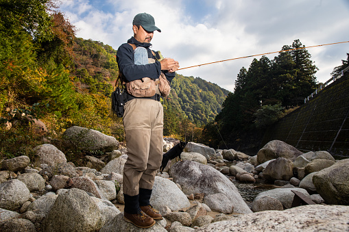 A Japanese man getting set up to do Fly fishing at a rocky creek in the mountains.