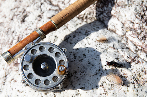A close up of a Fly Fishing rod, reel and some little fly hooks on a rock.