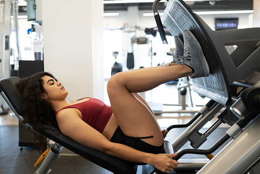 Side view of a fit young woman working out his quadriceps with a leg press machine at the gym