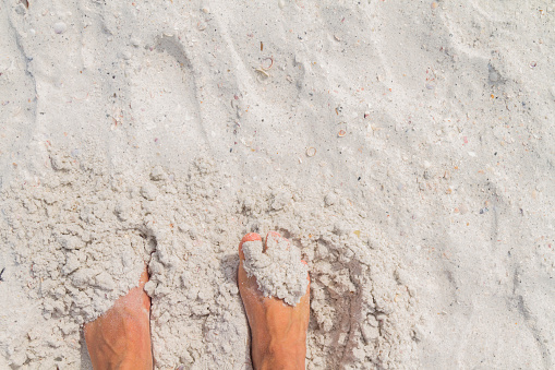 Feet on beach background. Top view on naked feet over the sand in Clearwater Beach, St. Petersburg, Florida, United States of America USA.\n\nHoliday, Summer and vacation holiday concept. Selfie male barefoot standing over white sand at the beach.