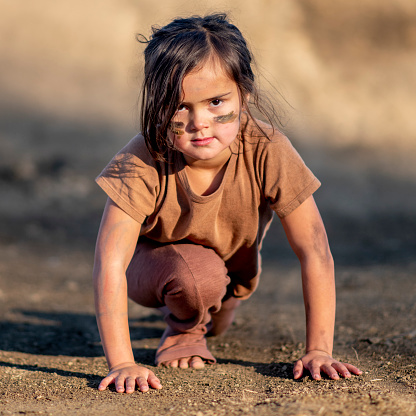 Little girl is ready to run and wearing brown against a brown dirt background.