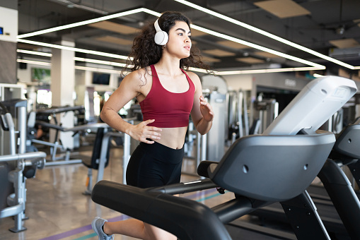 Attractive hispanic woman running fast on the treadmill while listening to music at a fitness center