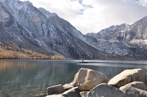Pretty fall colors, big boulders, fishing boat and reflections at Convict lake on a cloudy day in the autumn