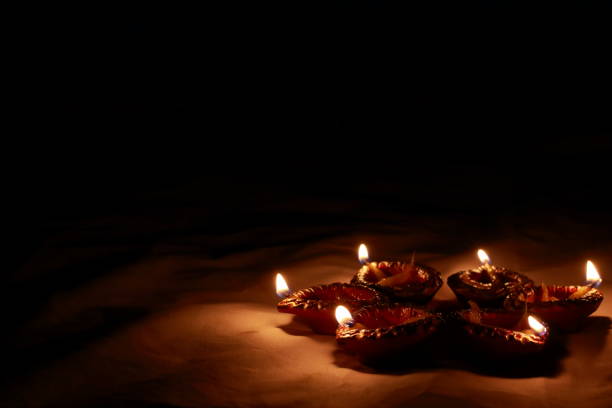 Indian traditional clay lamps with glowing flames kept together in a row during celebrations of indian hindu cultural festival of diwali or kali puja. photo taken with dark background and selective focus and shallow depth of field.concept depicting hope, good energy, peace. copy space background. close up shot. lámparas de arcilla tradicionales indias con llamas brillantes mantenidas juntas en una fila durante las celebraciones del festival cultural hindú indio de diwali o kali puja. copiar el fondo del espacio. foto tomada con fondo oscuro y enfoque selectivo