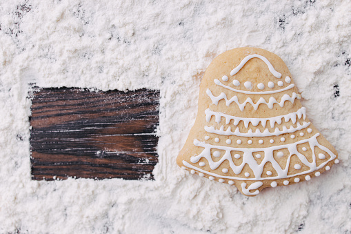 Christmas and New Year traditional attribute, festive sweets for kids, celebration mood. Homemade gingerbread bell cookie on wooden table