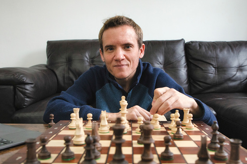 Close-up portrait of smiling trans autistic male over a chess board during a game.