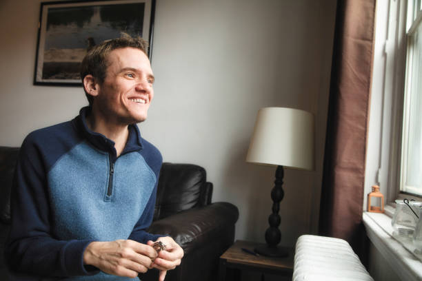 hombre trans autista en casa sonriendo mientras mira por la ventana - autism fotografías e imágenes de stock