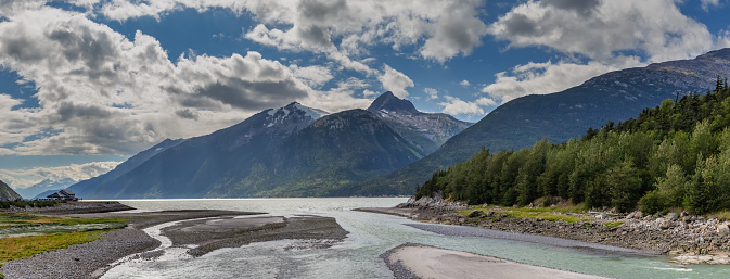 Panoramic shot of Yucatania point and shallow Skagway river in Skagway, Alaska. Mountains and cloudy blue sky as a background.