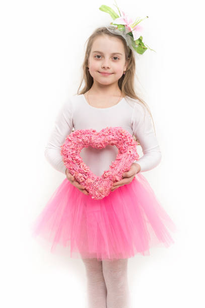Child smile with pink heart wreath isolated on white. Love, holiday, celebration. Valentines day concept. Christmas, new year, birthday. Girl with flower in long blond hair and skirt tutu.