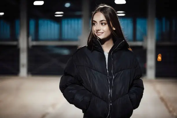 Bright smiling attractive young woman standing in underground carpark looking over to her friends. Real People Millennial Generation Lifestyle Portrait.