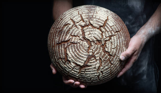 istock Baker's hands holding and presenting fresh baked loaf of bread 1285221088