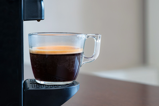 Close up of refreshing espresso pouring of capsule machine into a cup at home. Concept of coffee break.