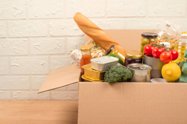 istock Donation box with different groceries, food donations on light background with copyspace - pasta, fresh vegatables, canned food, baguette, cooking oil. Food bank, food delivery concept 1285231612