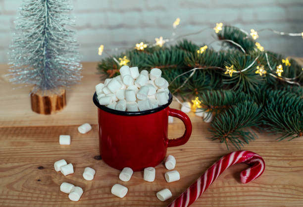 istock Hot chocolate cup with marshmallows with christmas lights and Christmas tree branches on the background 1285231987