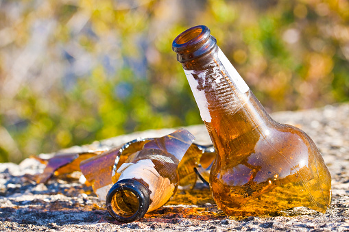 Shattered beer bottle resting on the ground: alcoholism concept - toned image