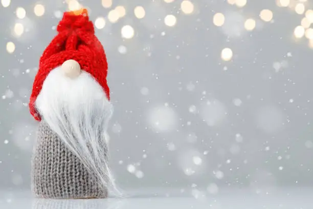 Photo of Knitted gnome with tree on gold background with yellow lights and snowflakes