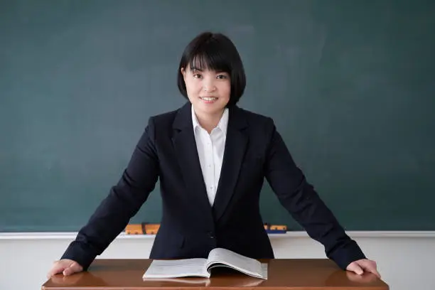 A Japanese woman teacher stands in front of the blackboard in her classroom