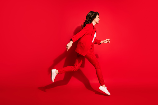 Full length profile photo of charming young girl fast running wear blazer pants footwear isolated red color background.