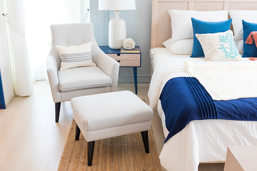 Close up of new comfortable bed with decorative pillows , wood headboard and side table lamp. Blue and orange scheme decoration.