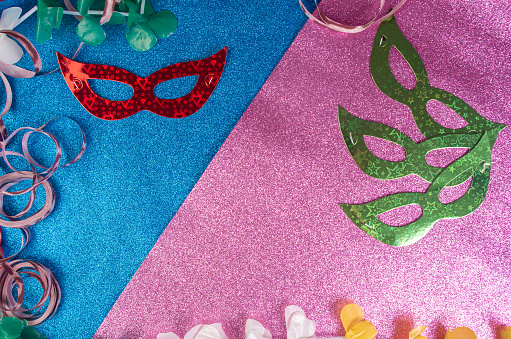 Brazilian carnival masks and props arranged on a pink and bright blue surface, top view.