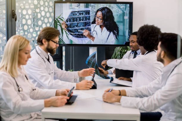 istock Team of multiracial experienced doctors or scientists, having video conference with their young confident African female expert and talking about the results of patient's CT during clinical trial 1285249623