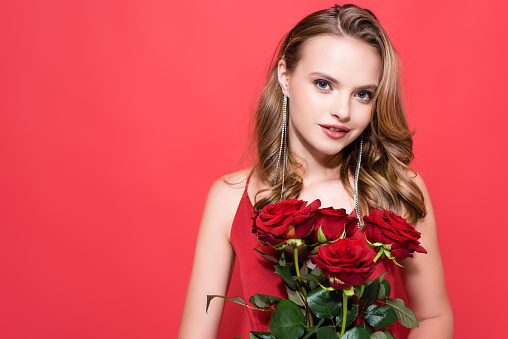 cheerful young woman holding roses and looking at camera on red