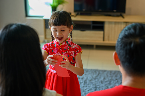 Happy Asian Chinese girl received red envelops from her parent during Chinese New Year at living room.