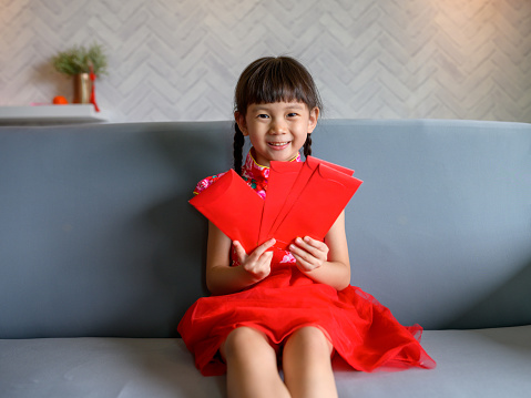 Lovely Asian Chinese girl holding red envelope with traditional dressing up celebrate Chinese new year in living room.