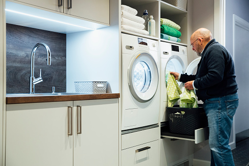 A senior male loading up the dryer with the towels that have just been washed he makes sure to choose the most energy-efficient cycle for what's been washed.